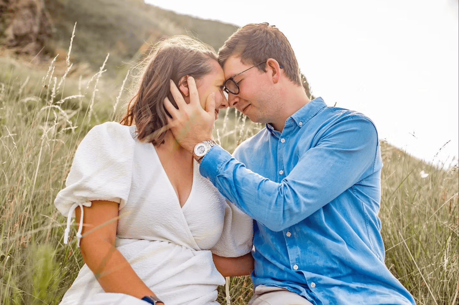 Couple sitting close together in golden meadow grass at sunset